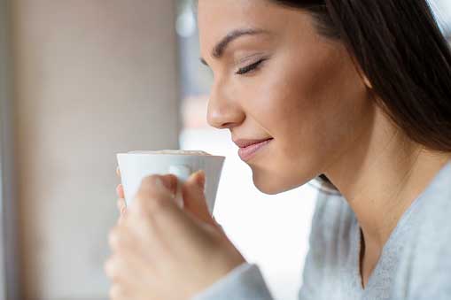Young, beautiful woman taking in the aroma from her coffee mug
